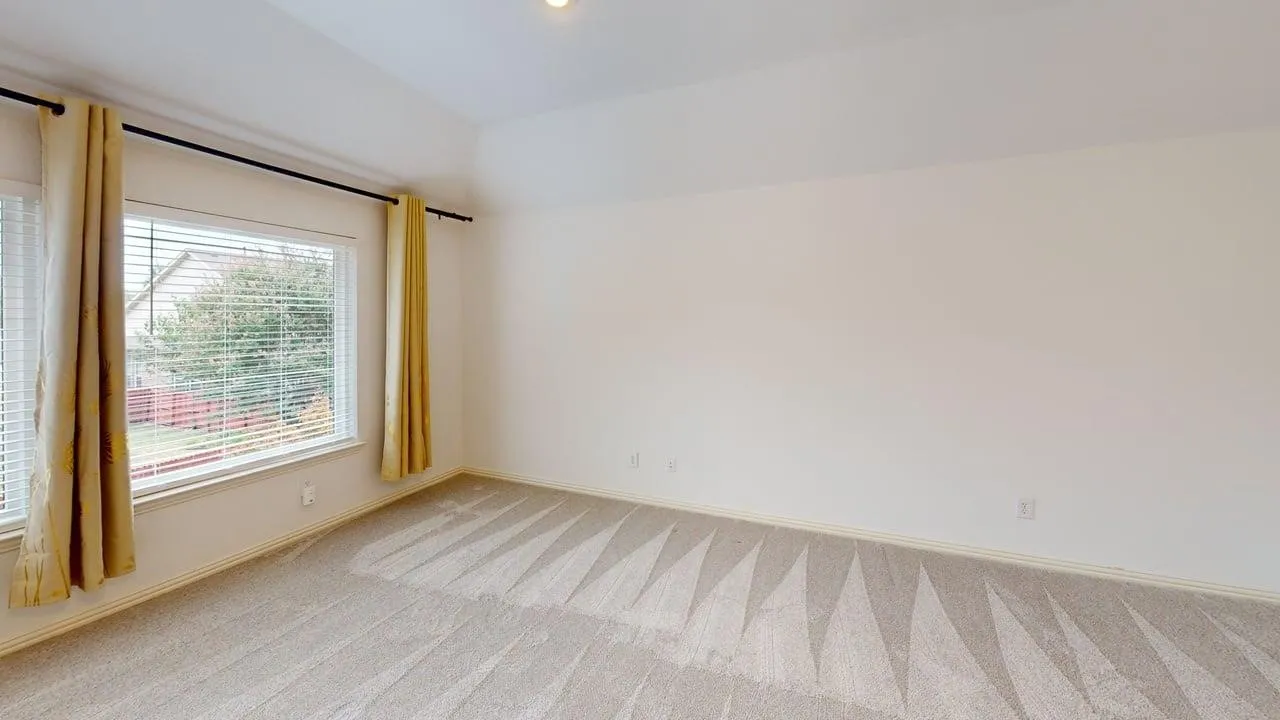 Light-colored carpeting, vaulted ceiling, and multiple windows with blinds