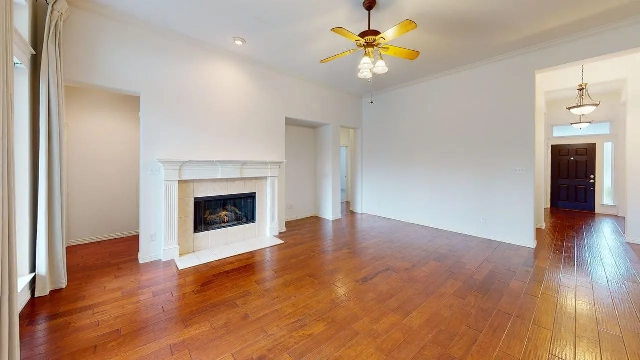 Wood-finish flooring throughout, a stone mantel fireplace with tile surround, a built-in ceiling fan, recessed lighting, and a dark wood entry door with transom and sidelight windows