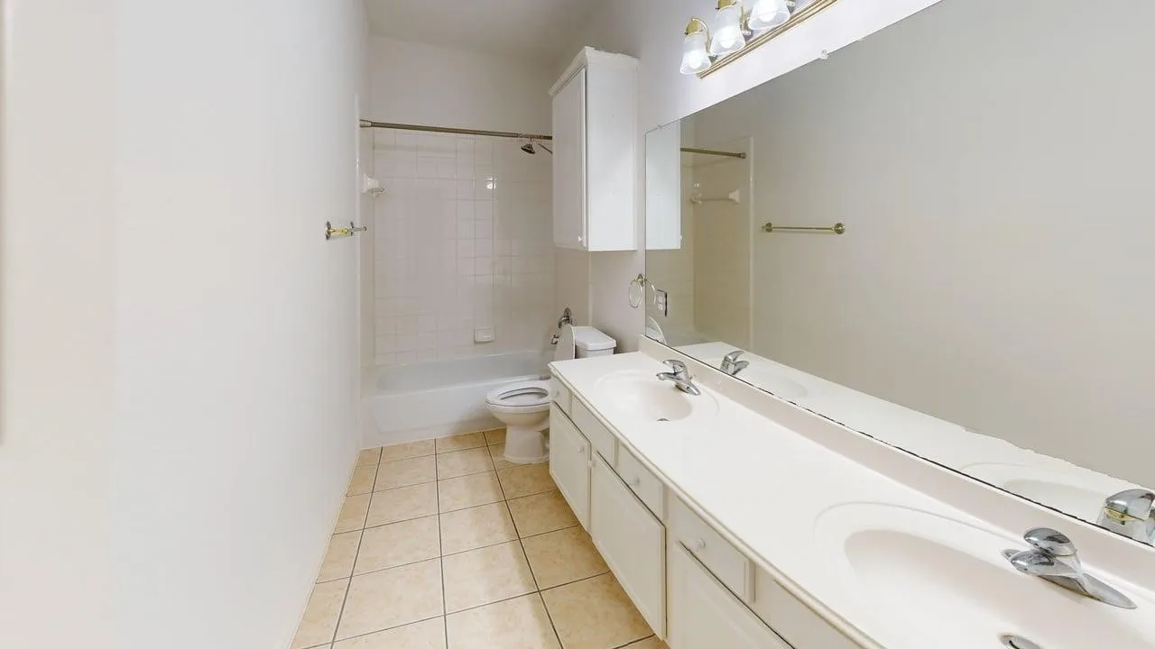 Dual vanity with integrated sinks, white cabinetry, a large mirror, and a tiled shower/tub combination