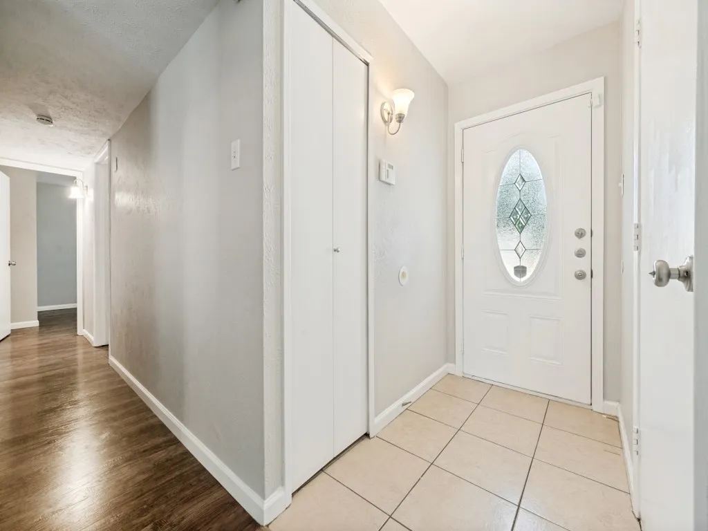 Entryway featuring a white door with decorative glass, wall-mounted sconce, and neutral tile flooring