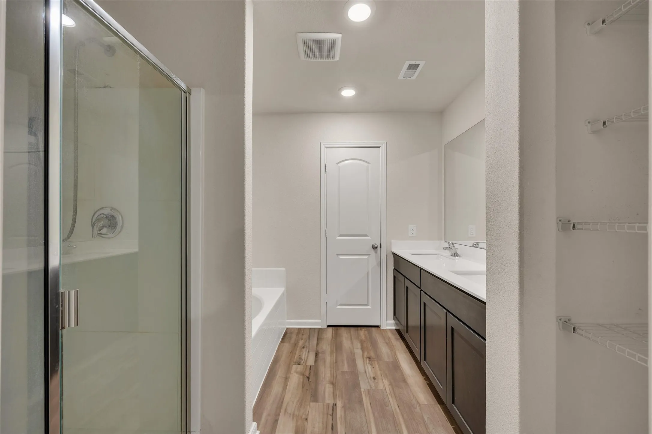 Glass-enclosed shower, built-in bathtub, dual vanity with undermount sinks, wood-finish flooring, and recessed lighting