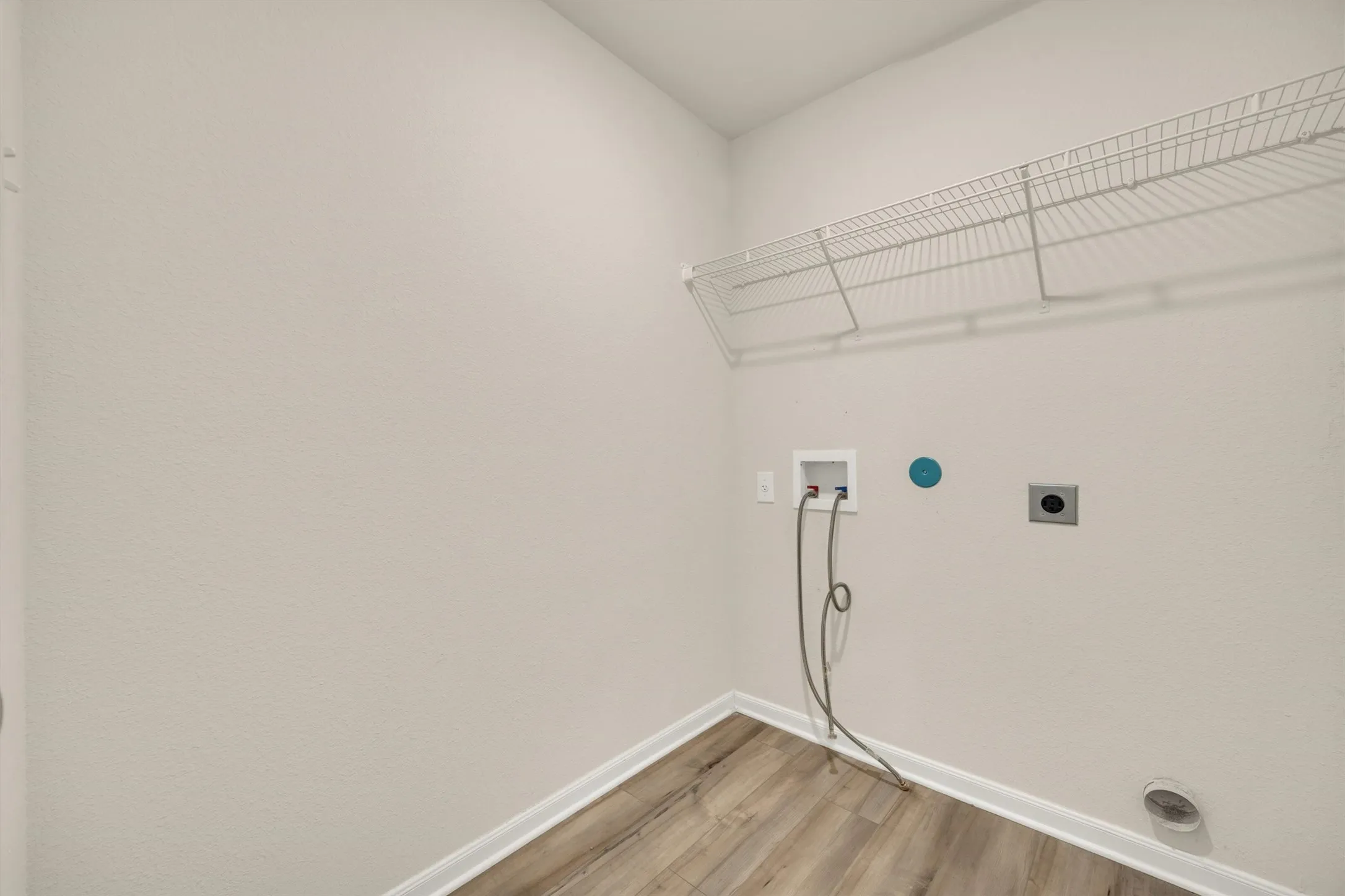 Utility room featuring wood-finish flooring, wire shelving, electrical outlets, and plumbing connections for washer/dryer hookup