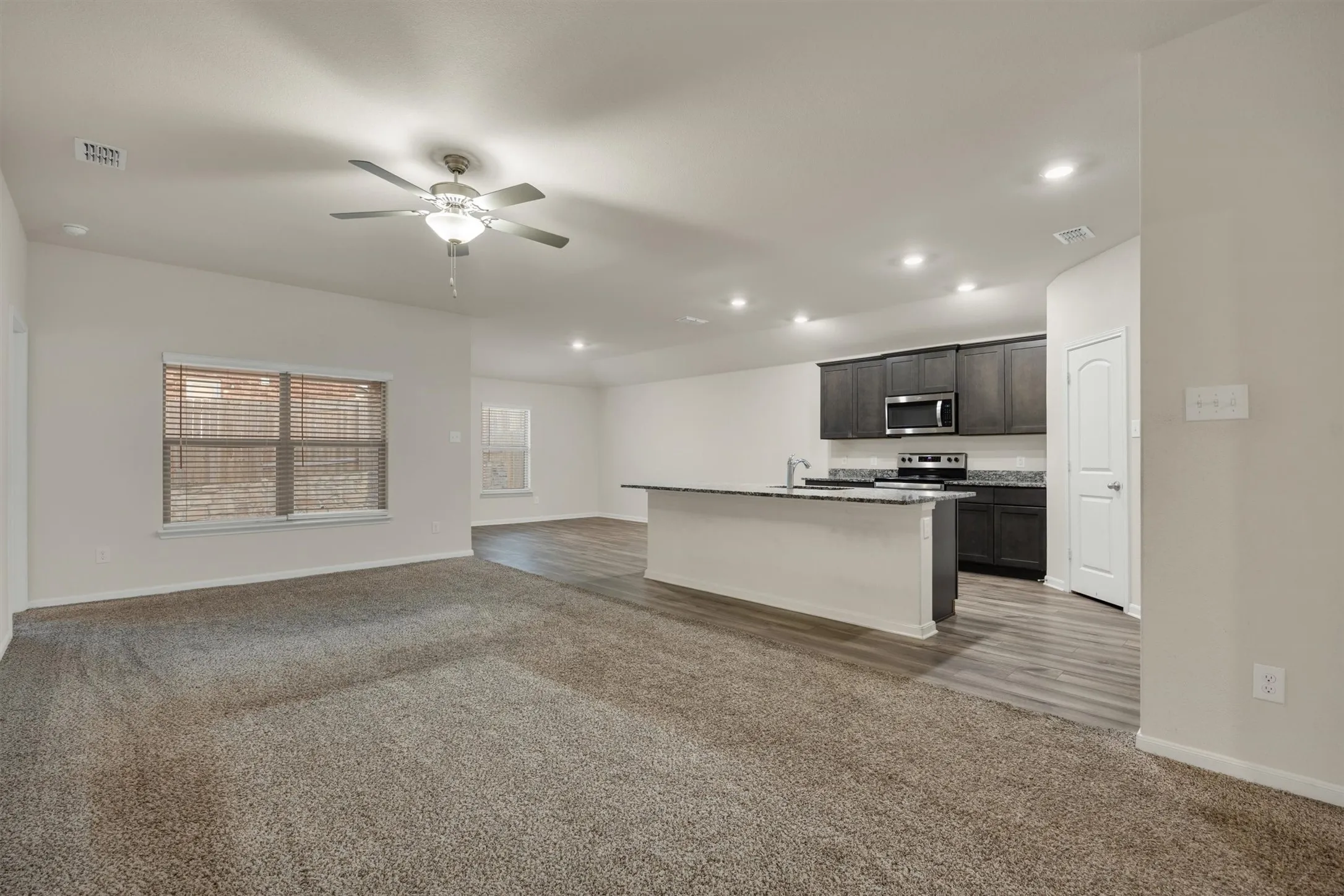 Spacious open-concept living area featuring soft carpet flooring, a ceiling fan, and recessed lighting
