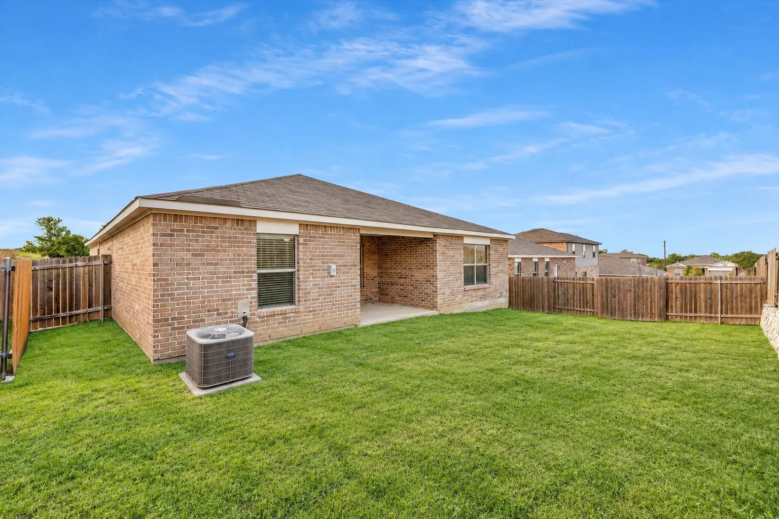 Expansive green lawn, full privacy fencing, brick exterior, covered patio, and central air conditioning unit