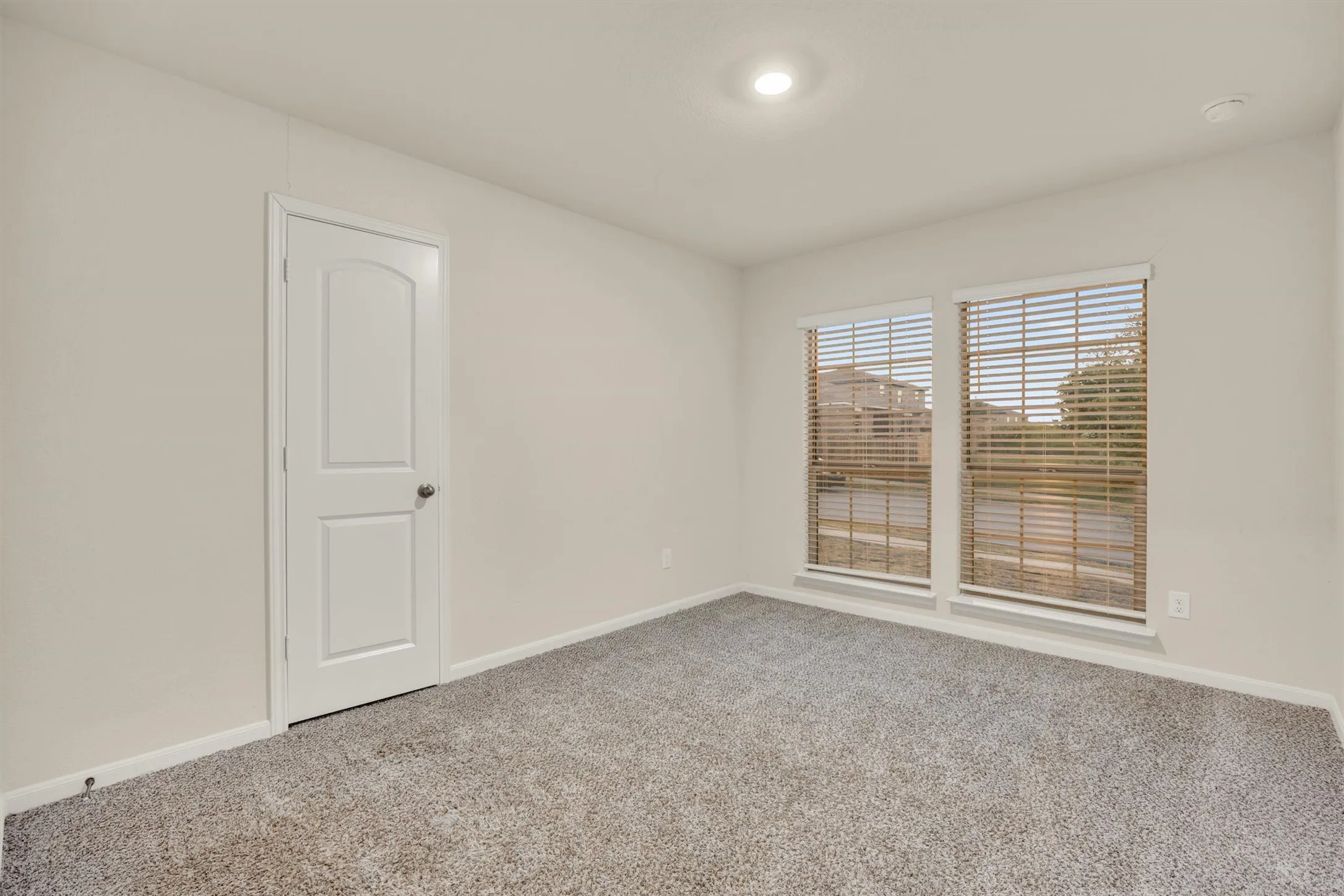 Plush carpeted flooring, neutral wall tones, two paneled windows with blinds, and recessed lighting