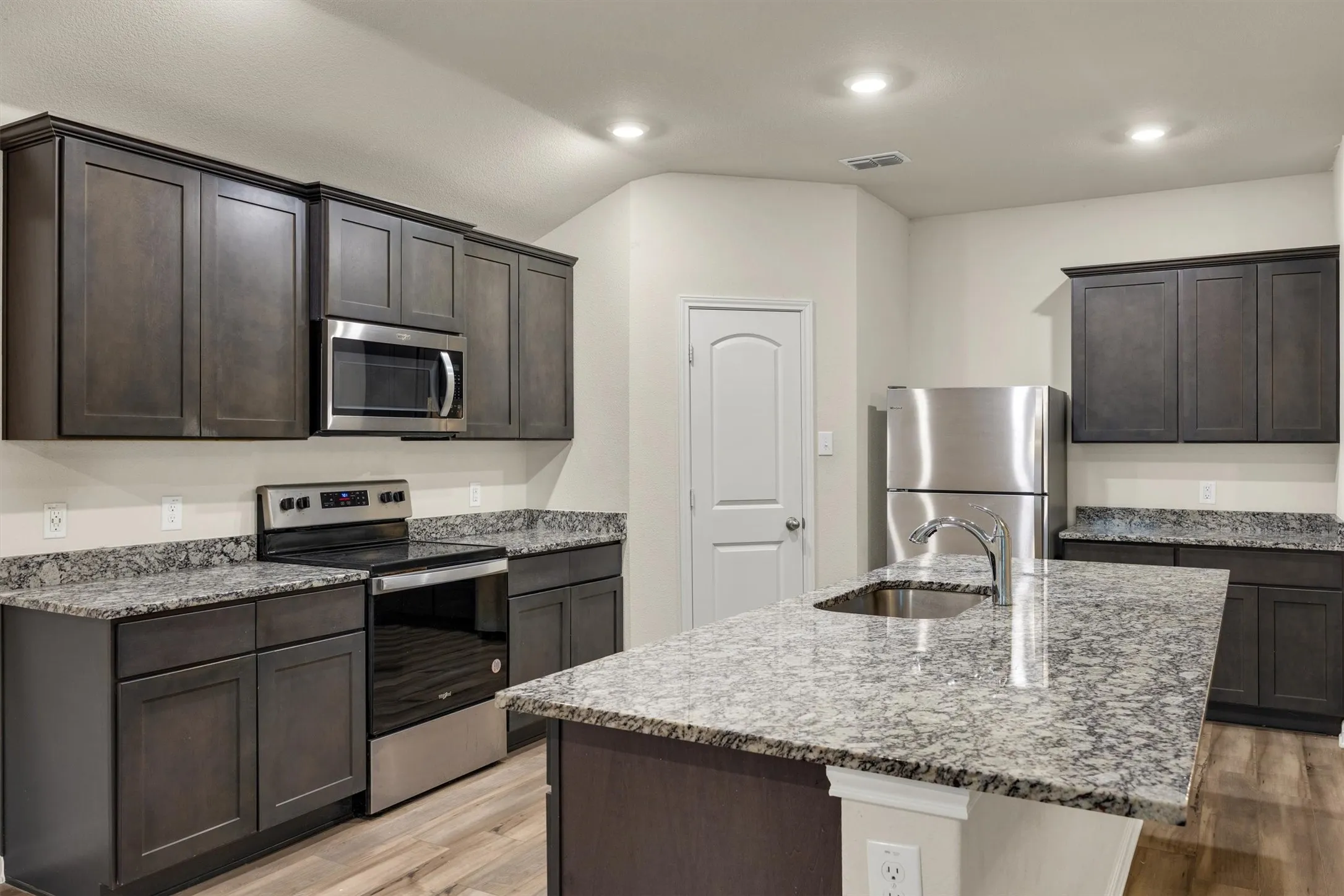 Kitchen featuring dark wood-finish cabinetry, granite countertops, stainless steel appliances, and a central island with an integrated sink