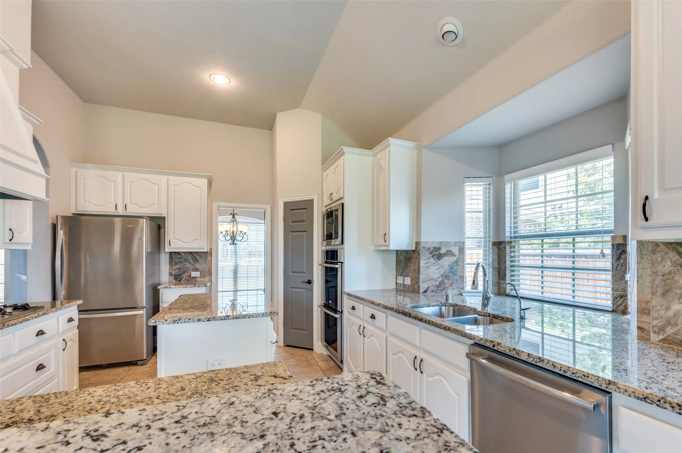 Stainless steel appliances, granite countertops, white cabinetry, built-in ovens, and a stainless steel sink with a high-arc faucet