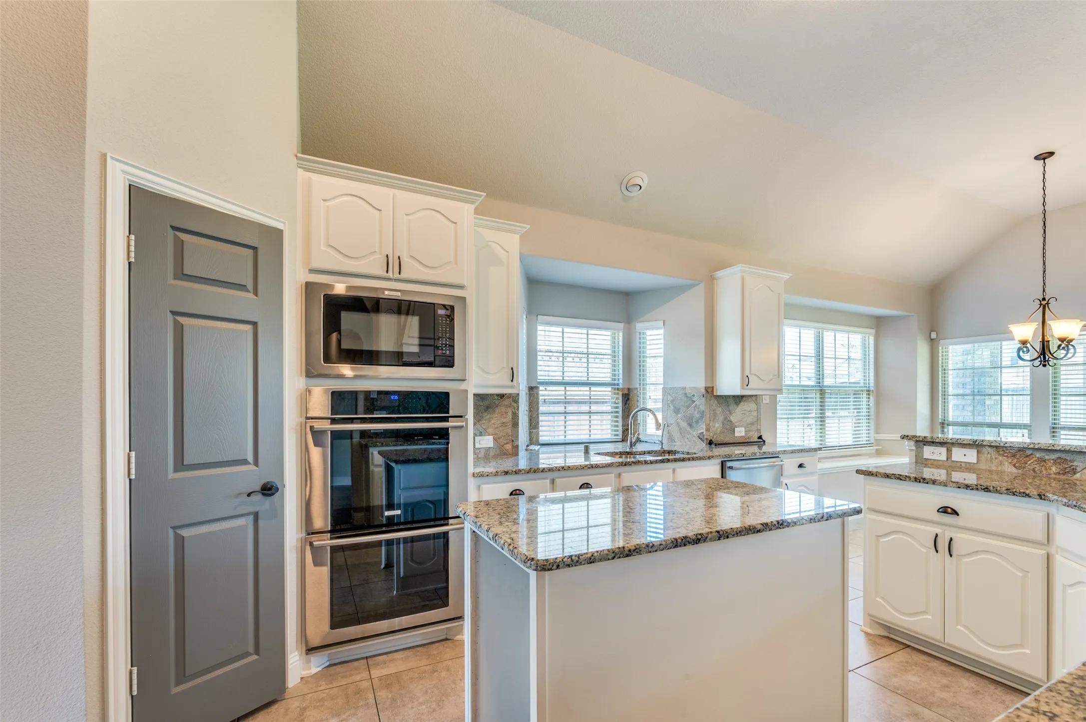 Kitchen featuring a center island with a granite countertop, white cabinetry, built-in stainless steel appliances, and a vaulted ceiling