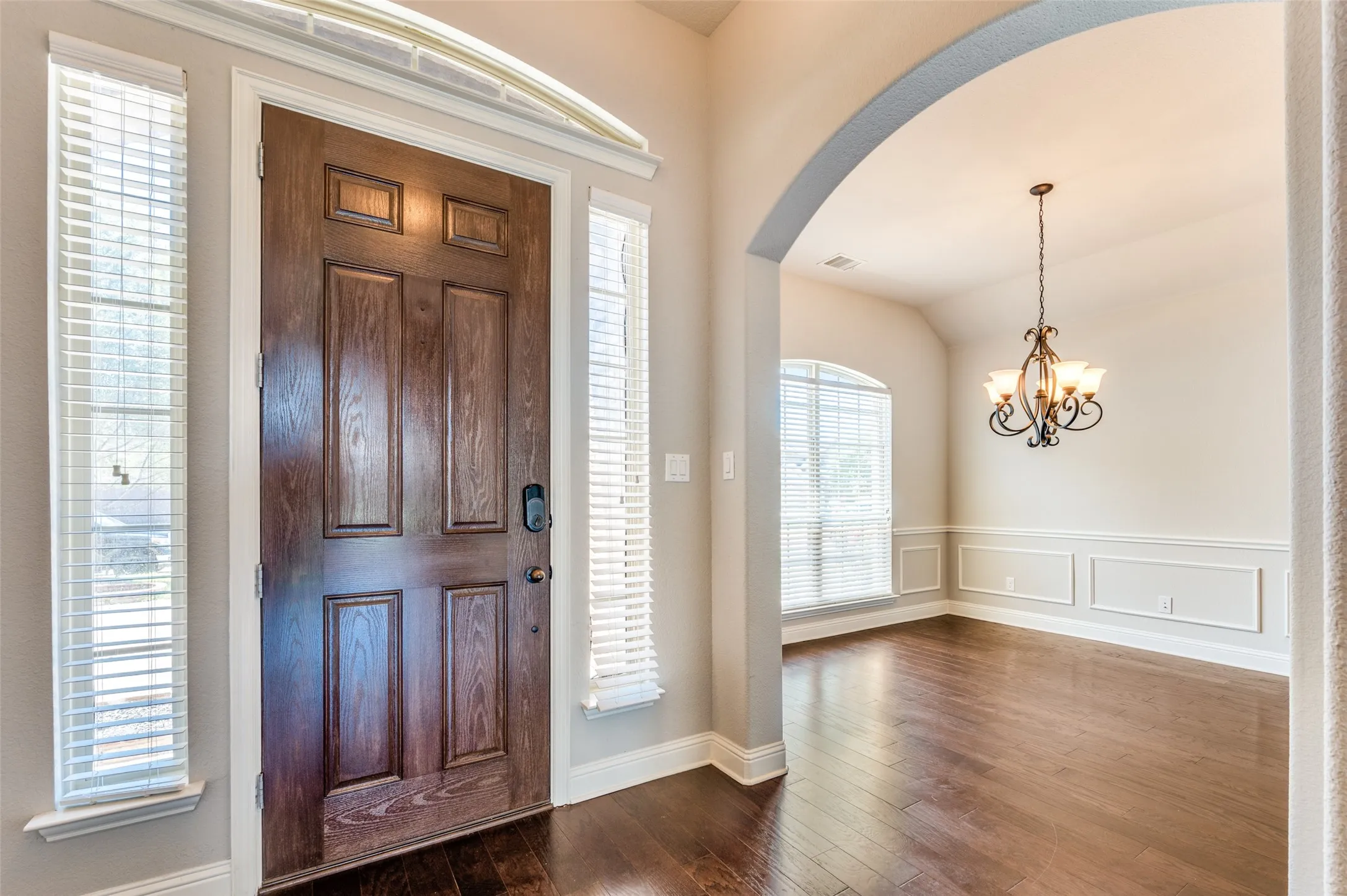 Wood-finish flooring throughout, arched entryway, decorative wainscoting, and a five-light chandelier