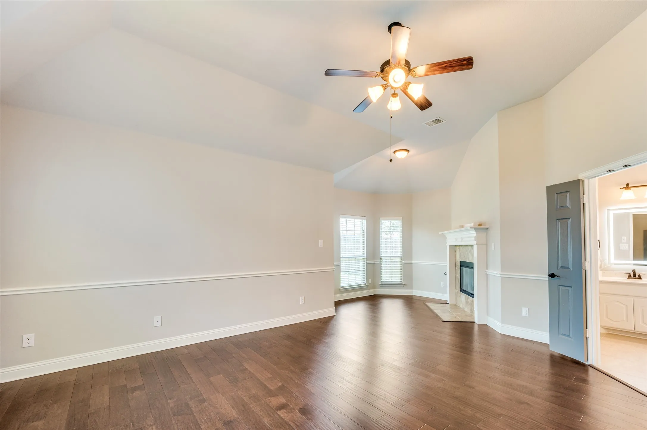 Vaulted ceiling with an attached ceiling fan, wood-finish flooring, and a fireplace with a mantel