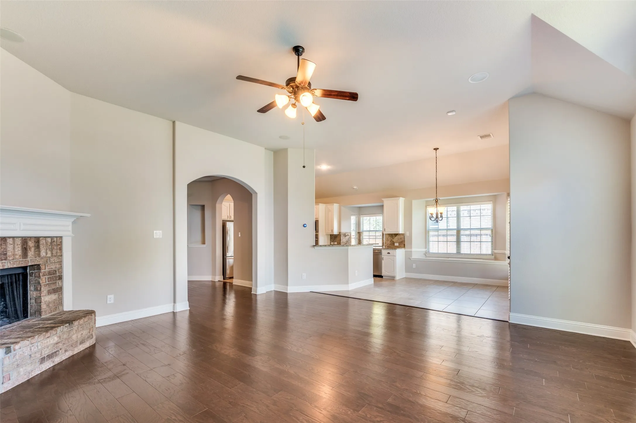 Vaulted ceilings, wood-finish flooring, brick fireplace with mantel, archway entry, and ceiling fan