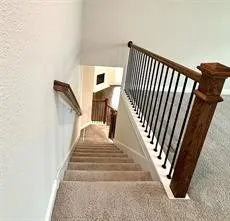 Carpeted staircase with wood handrail, black metal balusters, and painted risers