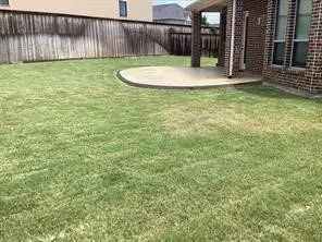 Expansive grassy yard with a covered patio featuring brick columns and a concrete slab