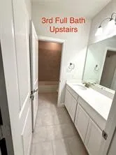 White vanity with integrated sink, expansive mirror, wall-mounted light fixture, and tile flooring