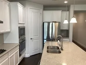 Modern kitchen featuring white shaker cabinetry, stainless steel appliances, a double basin sink, light-toned countertops, and pendant lighting