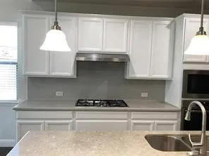 White shaker-style cabinetry, stainless steel range hood, built-in gas cooktop, undermount sink, and pendant lighting
