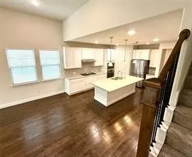 Open-concept living area featuring a kitchen island with sink, stainless steel appliances, dark wood-finish flooring, and a staircase with wood newel post and balusters