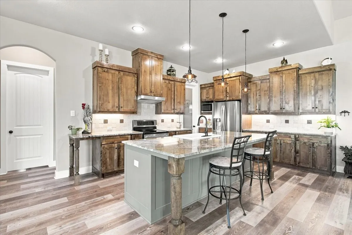 Kitchen featuring wood-finish flooring, custom wooden cabinetry, a center island with countertop seating, stainless steel appliances, and recessed lighting