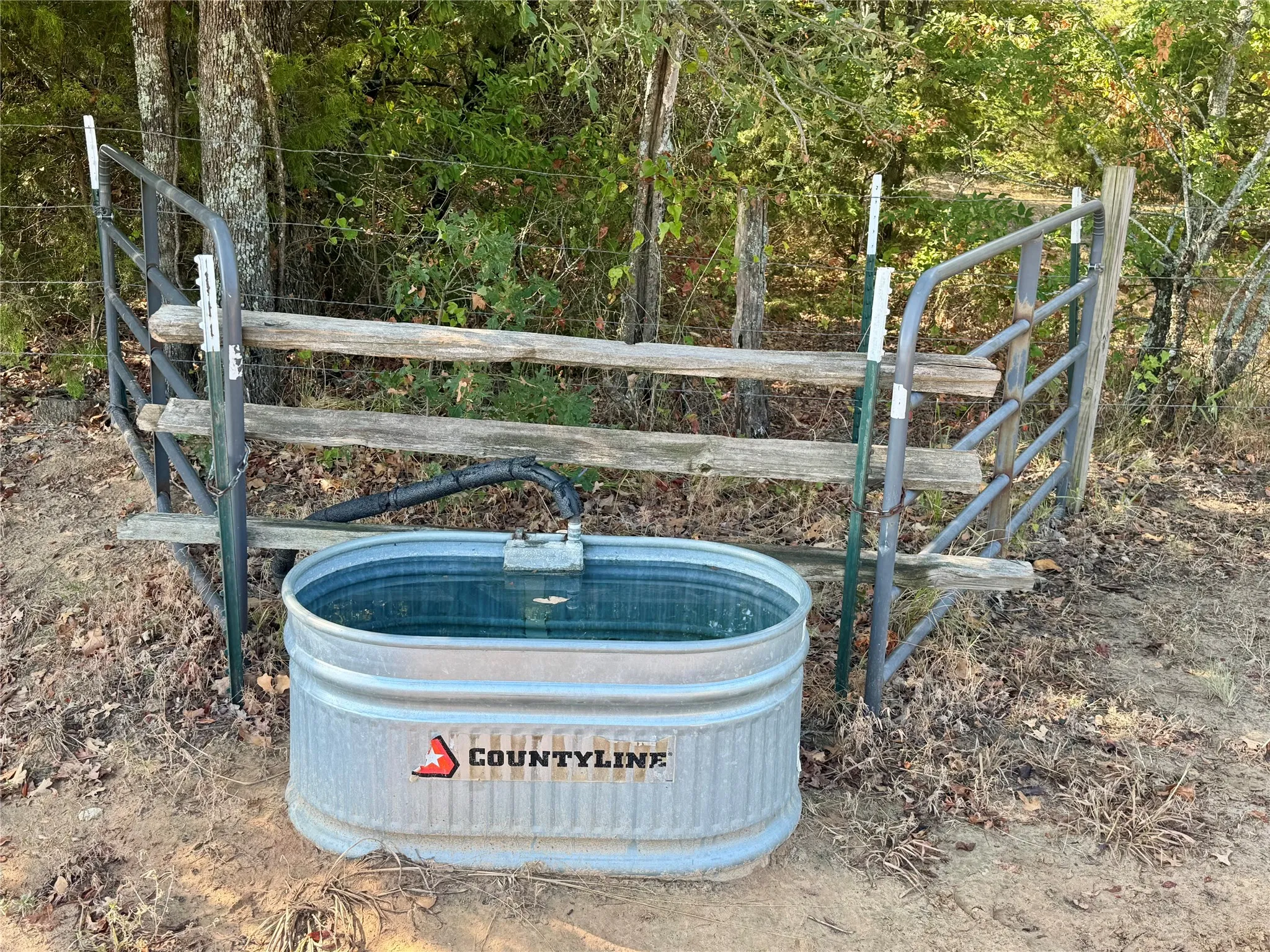 Galvanized stock tank with water, metal gate, and wooden fence