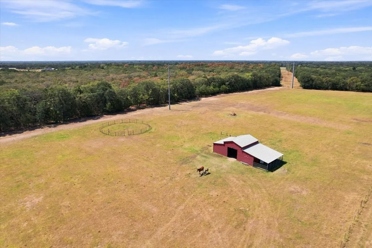 Expansive open fields with a red barn featuring a covered lean-to, and a round pen