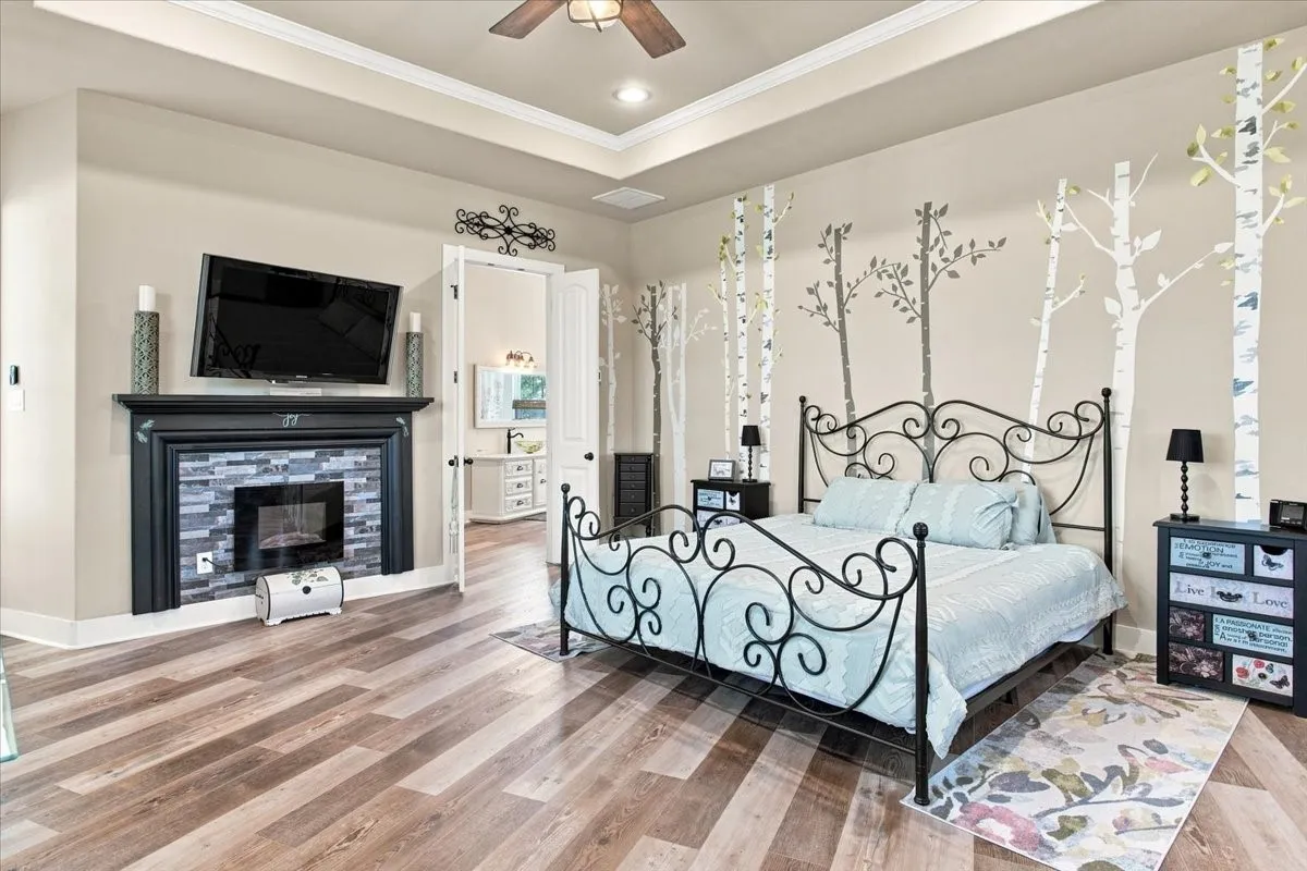 Tray ceiling with crown molding, wood-finish flooring, built-in fireplace with a stone-tile surround, black mantel, and television mounting
