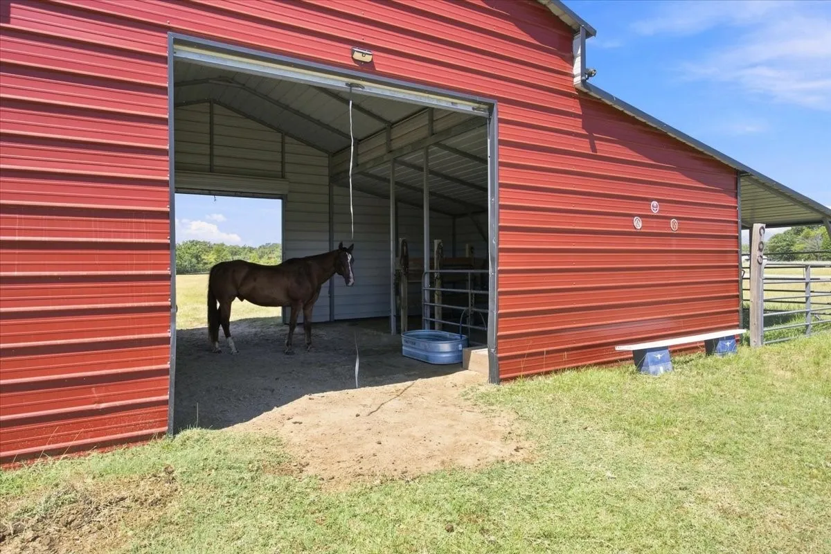 Red corrugated metal barn with an open bay, interior metal framing, and a partially visible covered extension