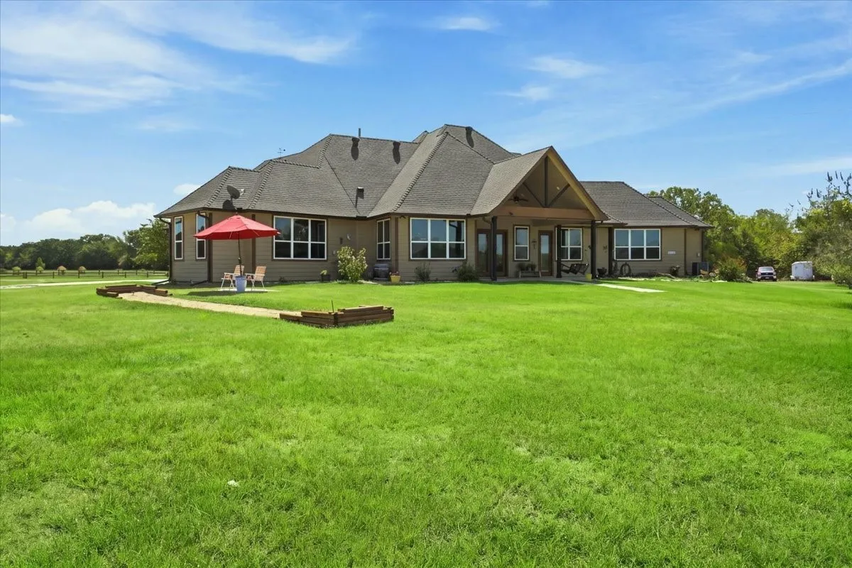Expansive green lawn surrounds the residence, featuring a covered patio with exposed beam details, and multiple windows