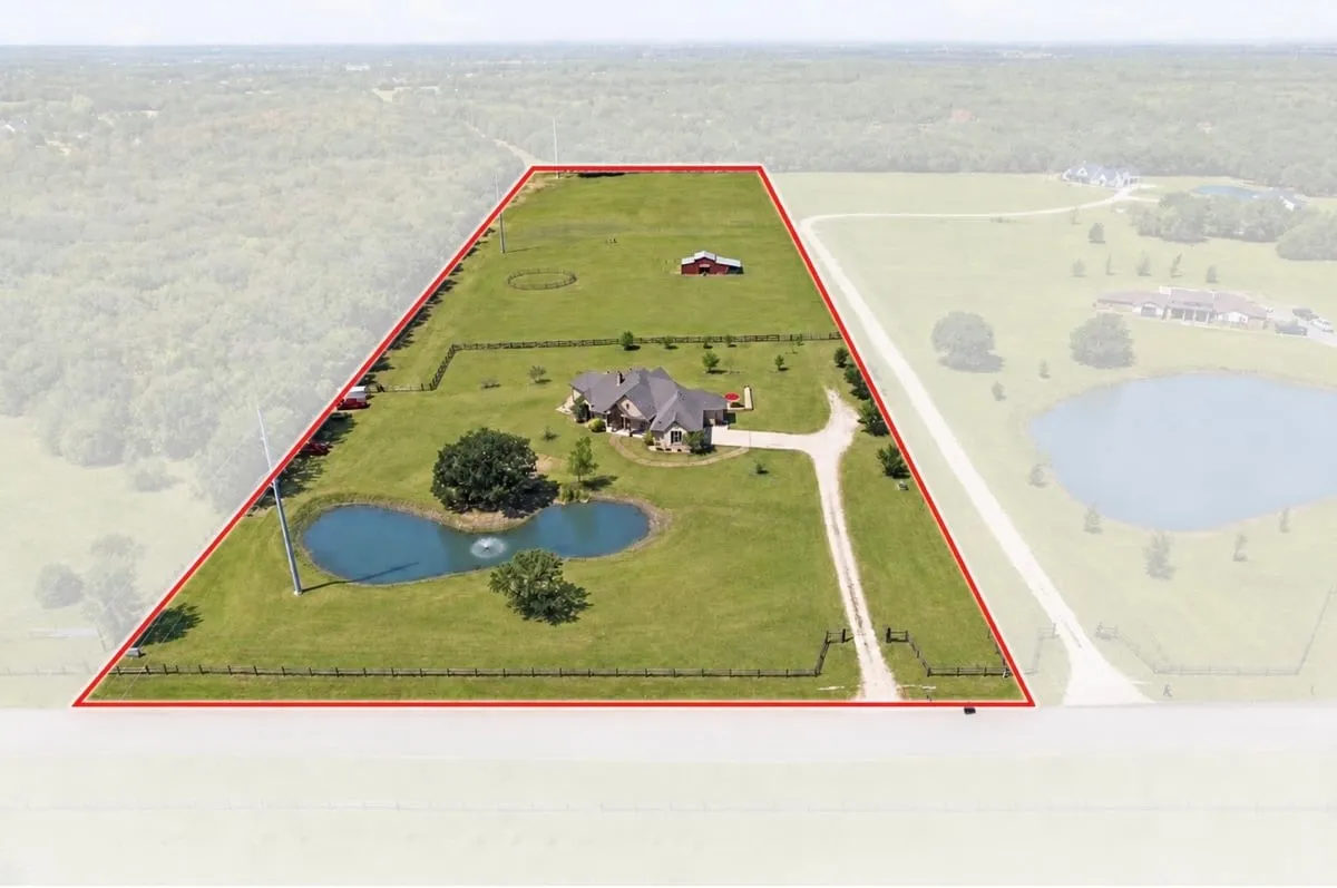 Expansive property featuring a residence, detached red barn, two ponds with one fountain, and a gravel driveway