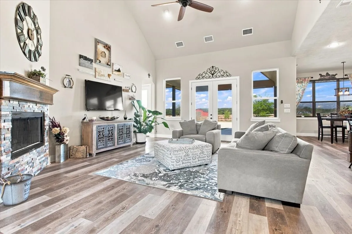Vaulted ceilings, wood-finish flooring, stone-clad fireplace with wood mantel, double French doors, and ceiling fan