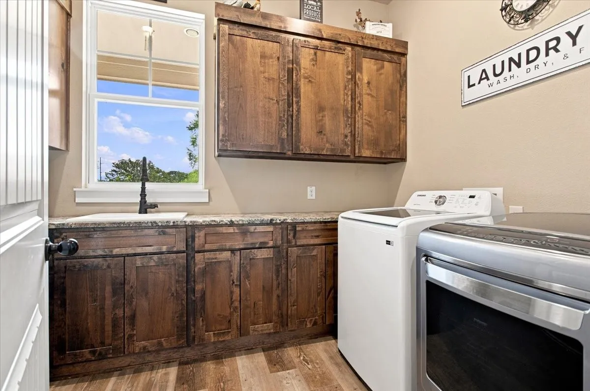 Laundry room featuring wood-finish flooring, dark wood-tone cabinetry, a utility sink with a matte black faucet, and a light-colored countertop