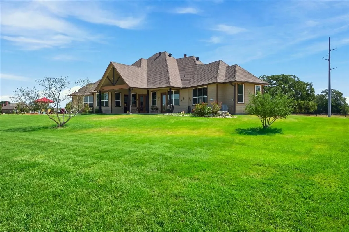 Expansive backyard with a manicured lawn, a covered patio, multiple windows, and a multi-level roofline