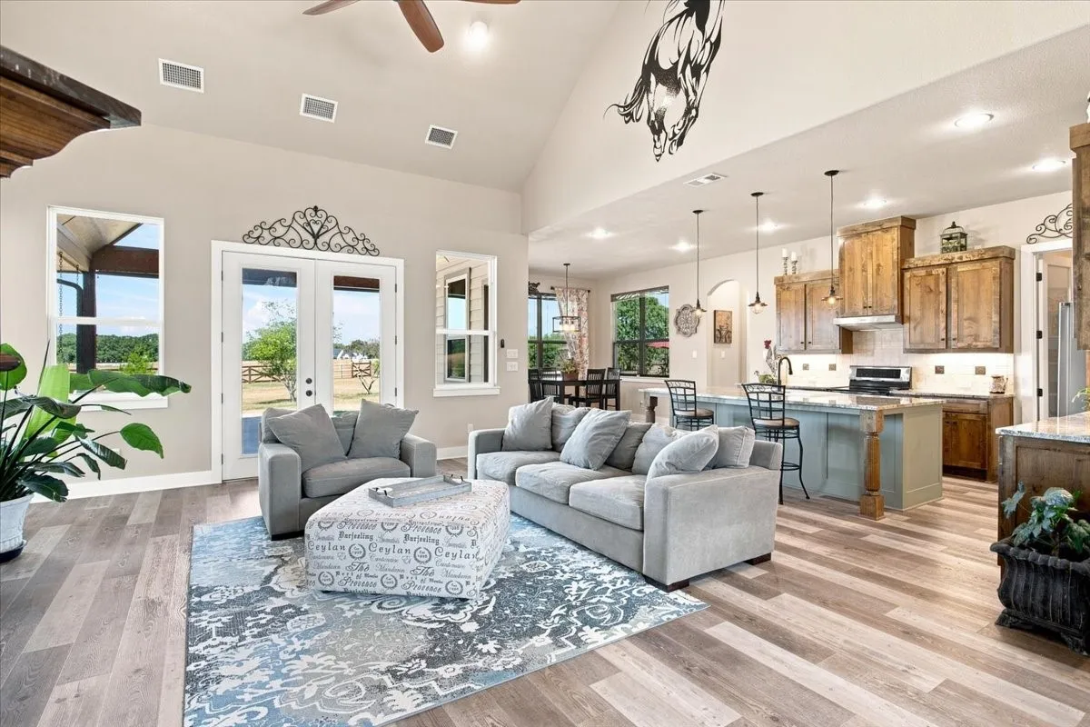 Vaulted ceiling with recessed lighting and a ceiling fan, wood-finish flooring, double glass panel doors, and a kitchen featuring a central island with bar seating, pendant lighting, and wood cabinetry