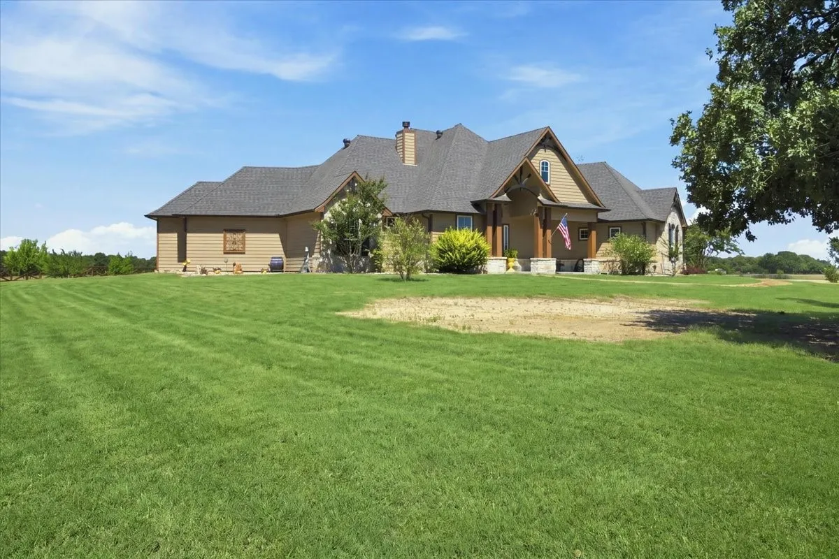 Expansive front lawn with mature landscaping, a stone and siding exterior, a prominent gable roof, and a covered entry with wood columns