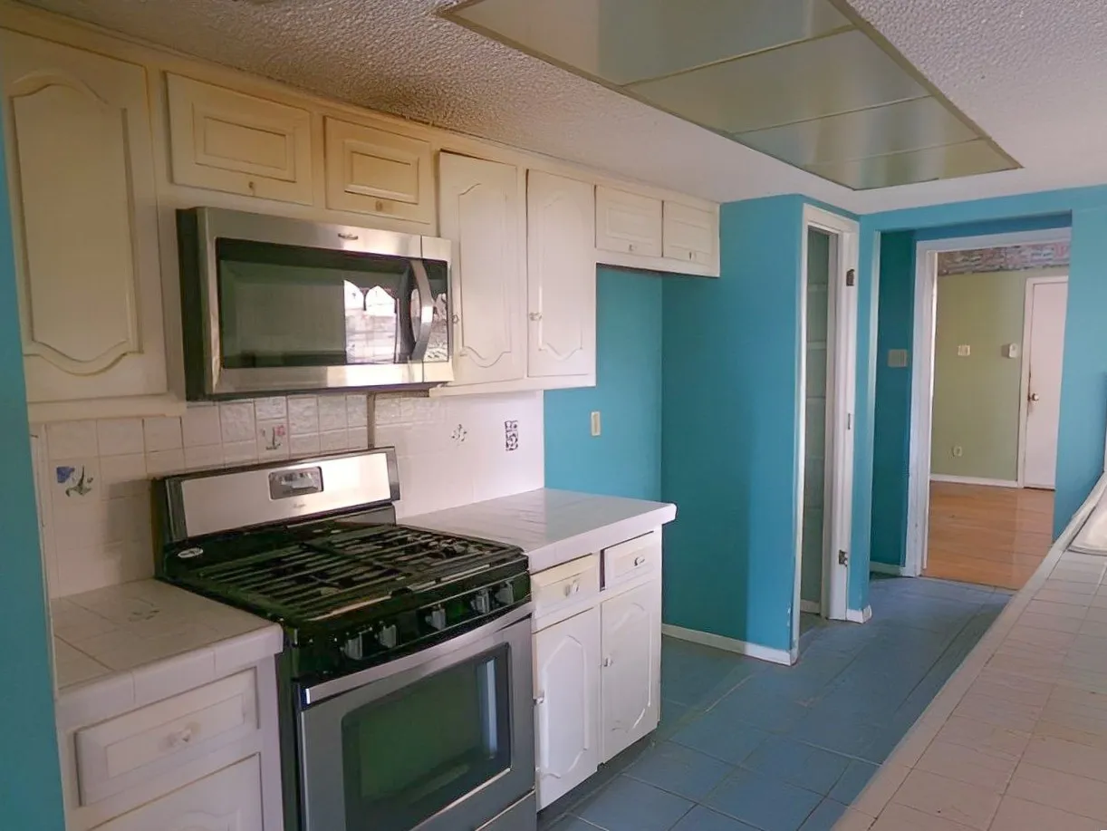 Kitchen featuring white cabinetry, stainless steel microwave, stainless steel gas range, tiled countertops, and tiled flooring