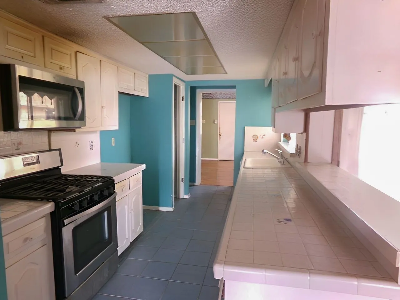 Kitchen featuring white cabinetry, tile countertops, stainless steel microwave, gas range, and tile flooring