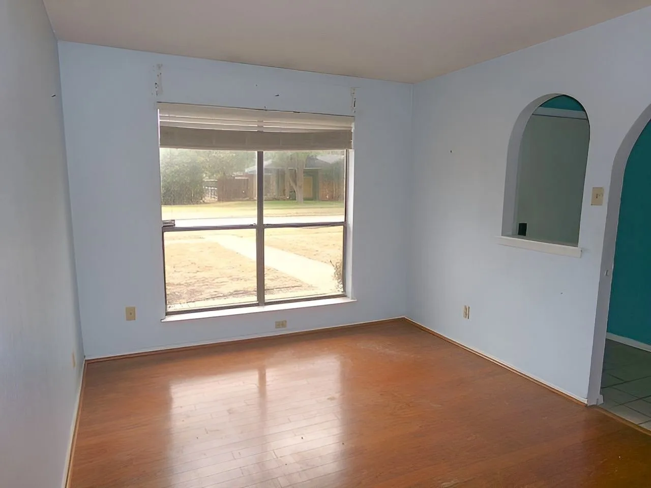 Formal living room Expansive window, wood-finish flooring, light blue wall paint, arched pass-through opening, and a wall cutout