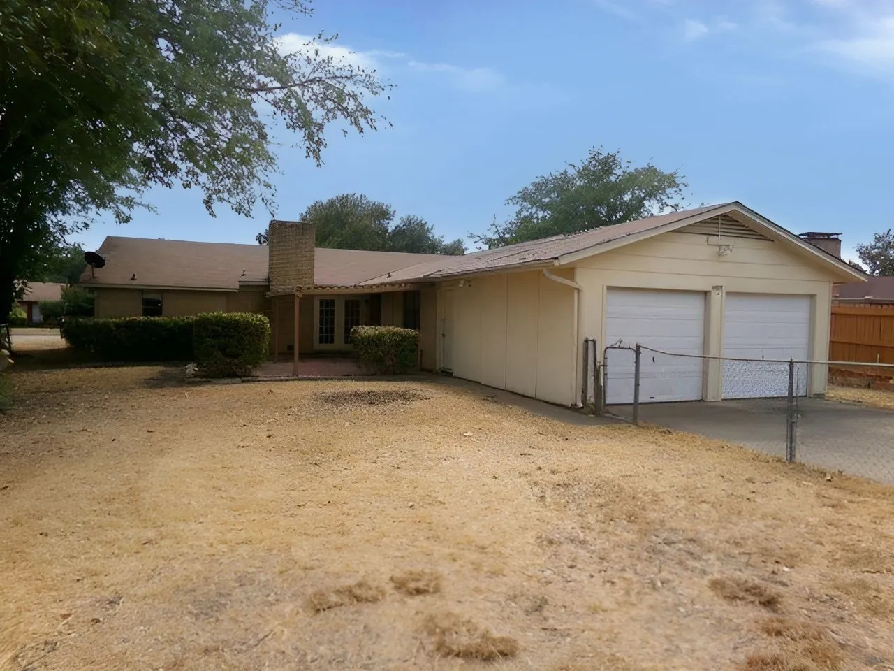 Two-car garage with white doors, exterior brick chimney, and a rear patio with brick-look flooring