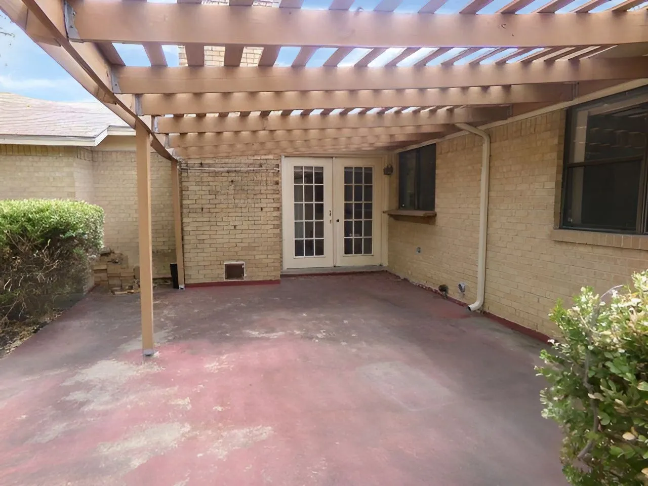 Paved patio area featuring a slatted pergola, brick exterior, and white French doors