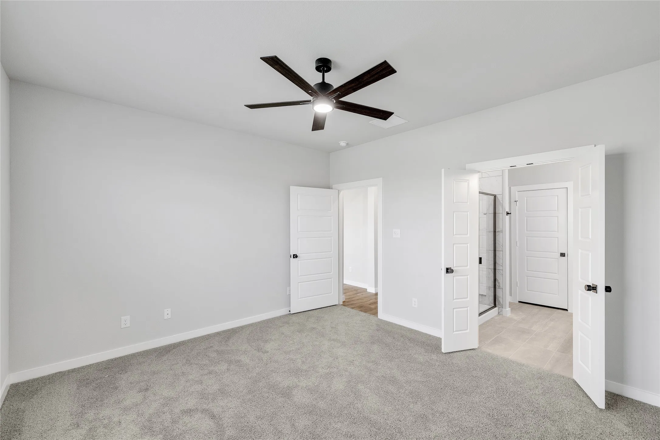 Plush gray carpet, white interior doors with matte black hardware, and a dark-bladed ceiling fan