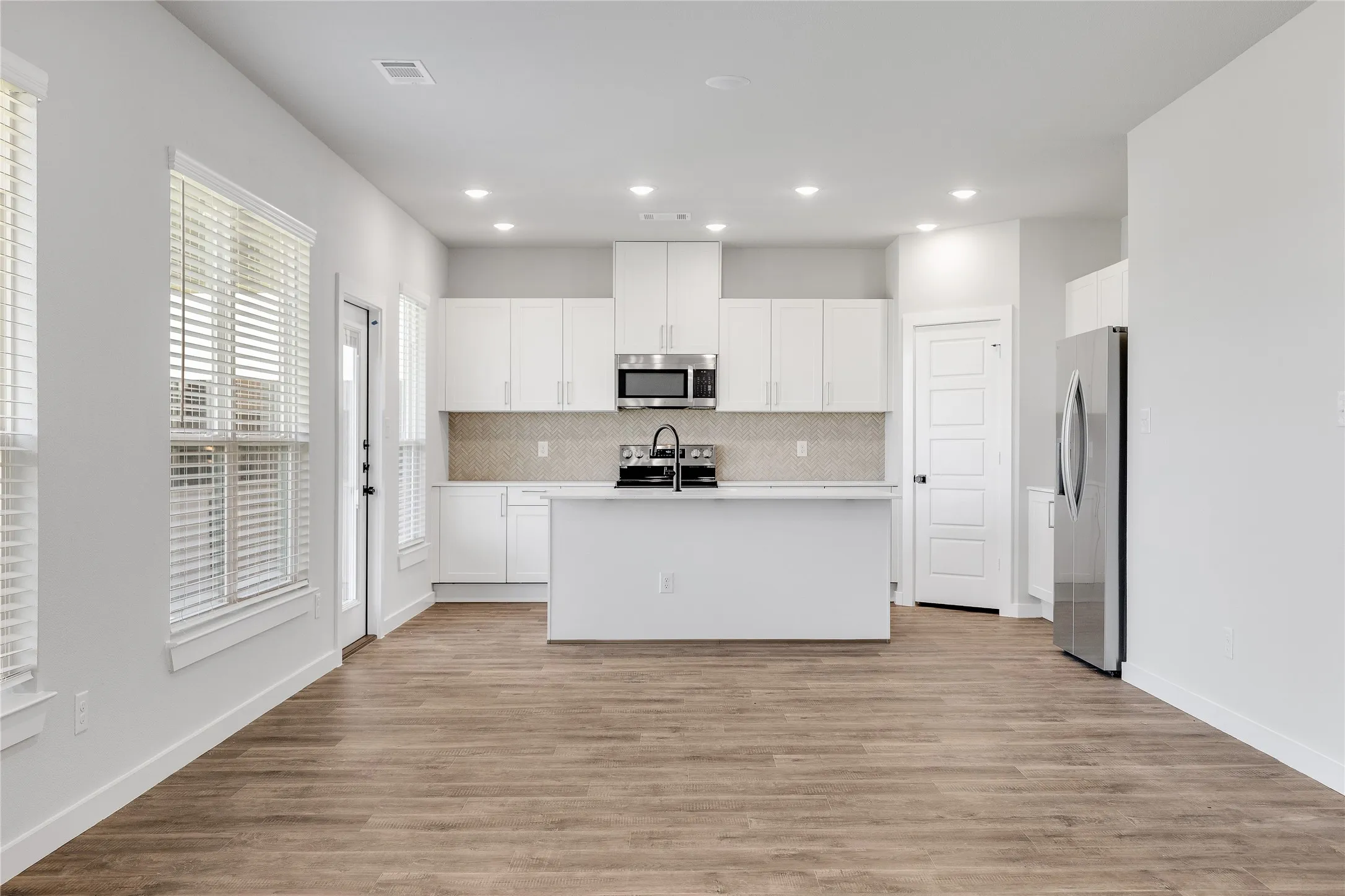 Modern kitchen featuring white cabinetry, stainless steel appliances, a center island, and wood-finish flooring