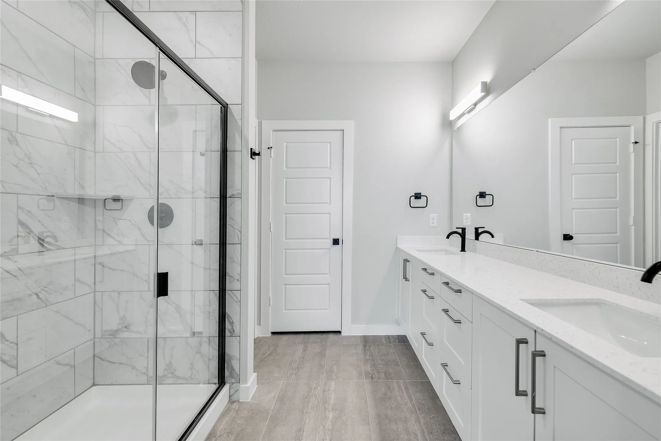 Walk-in shower with clear glass enclosure, dual vanity with solid surface countertops, and wood-finish flooring