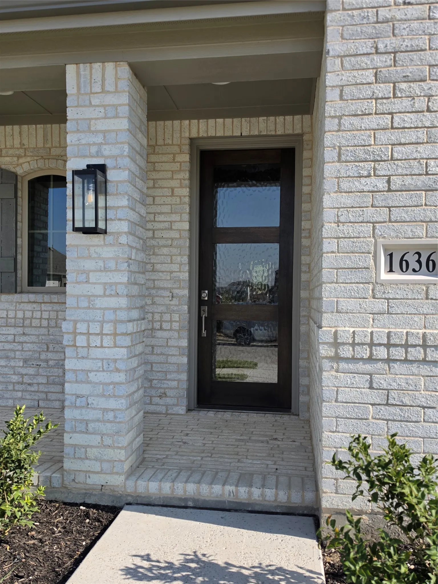 Brick exterior with a covered entry, dark-frame door featuring privacy glass, and a modern exterior light fixture