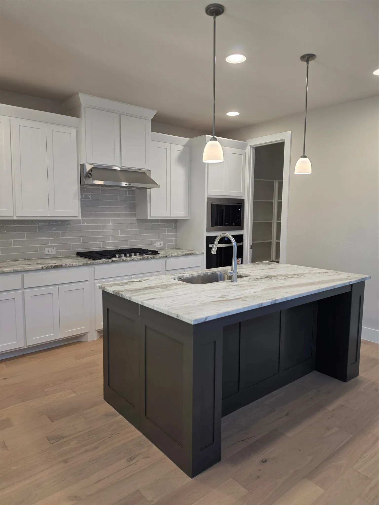 Kitchen featuring a large island with sink, light-toned wood-finish flooring, white cabinetry, integrated microwave, and pendant lighting