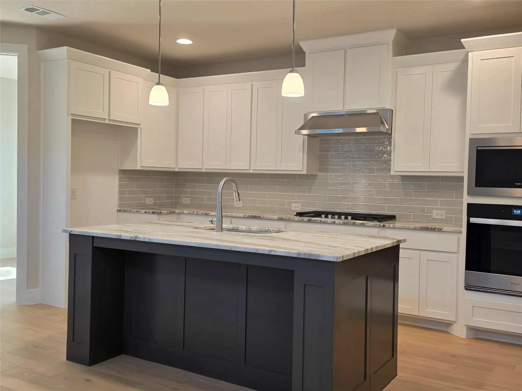 Kitchen featuring a central island, white shaker cabinetry, stainless steel appliances, and light wood-finish flooring