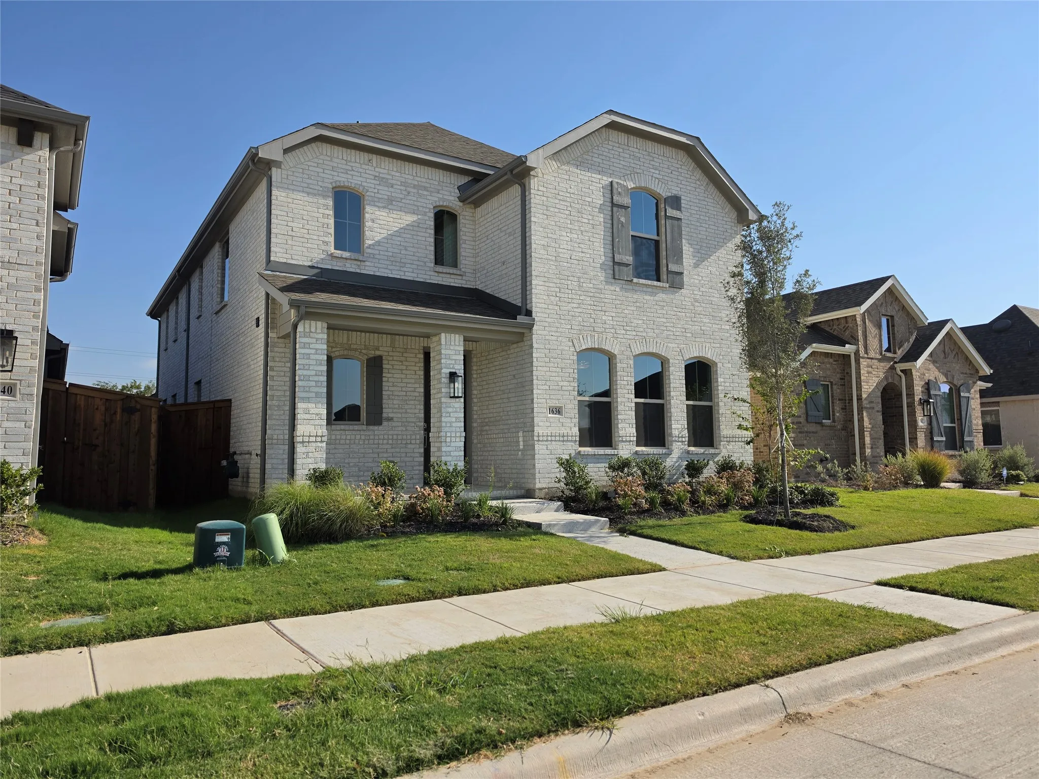 Two-story brick exterior, covered front porch, arched windows, decorative window shutters, and landscaped front yard