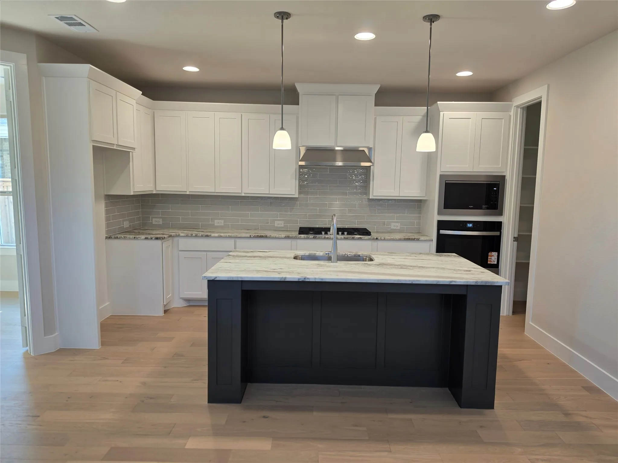 Kitchen featuring a dark-toned island with a light-toned countertop, white cabinetry, integrated stainless steel appliances, a tile backsplash, and light wood-finish flooring