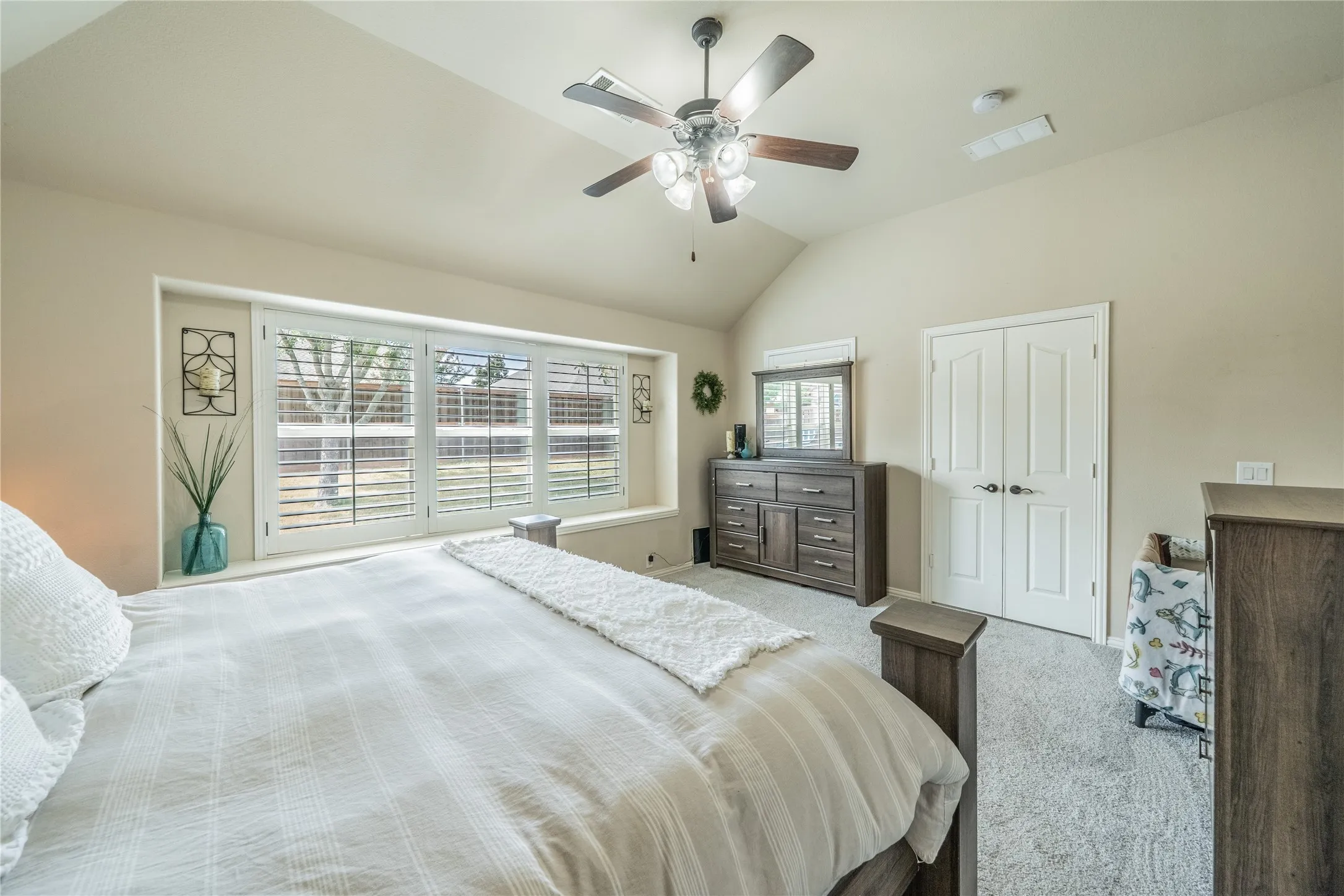 Vaulted ceiling with a ceiling fan light fixture, large windows with plantation shutters, window seat, and carpeted flooring