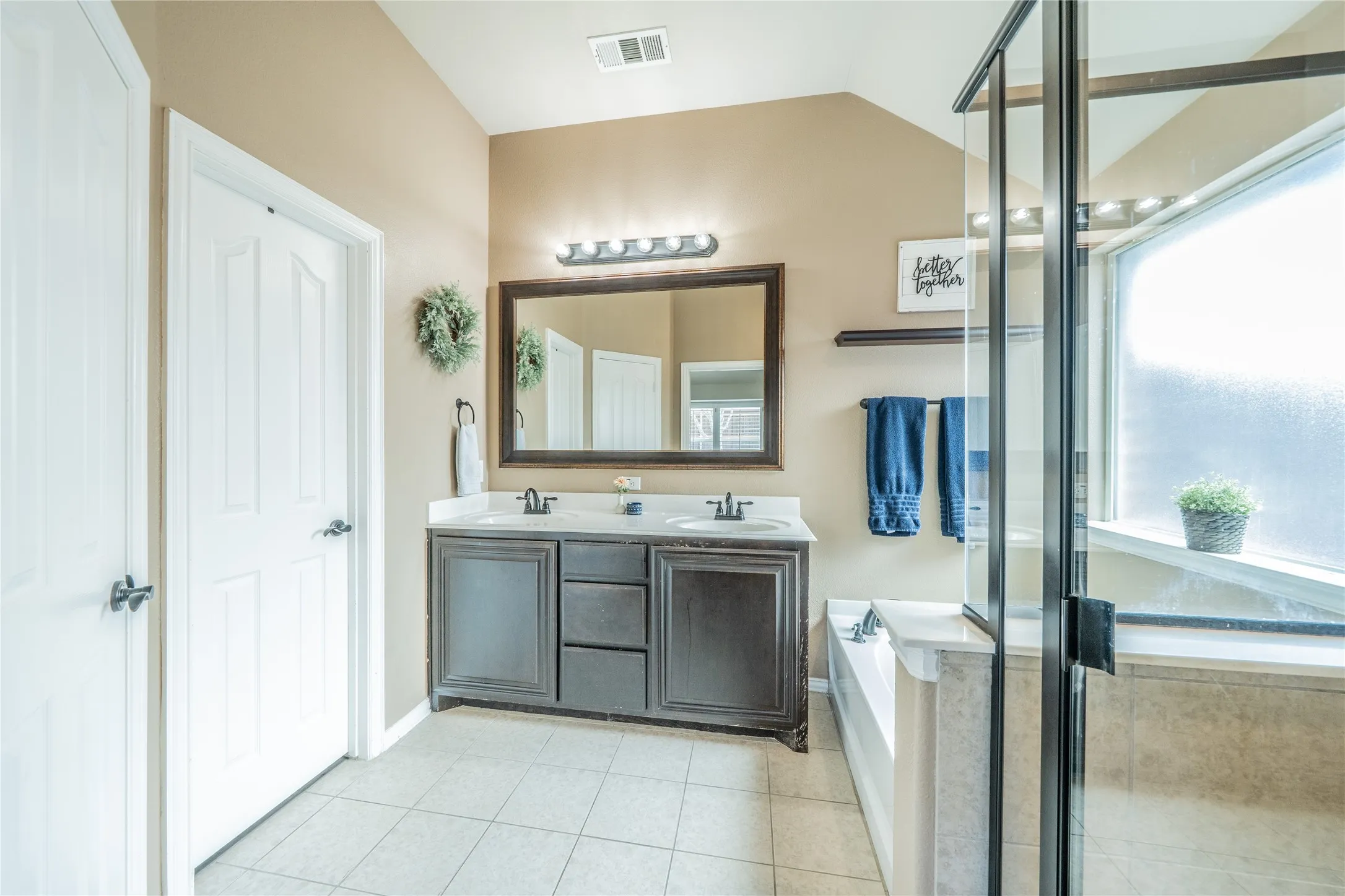 Double vanity with dark wood-finish cabinetry and white countertops, accented by a framed mirror and wall-mounted lighting fixture