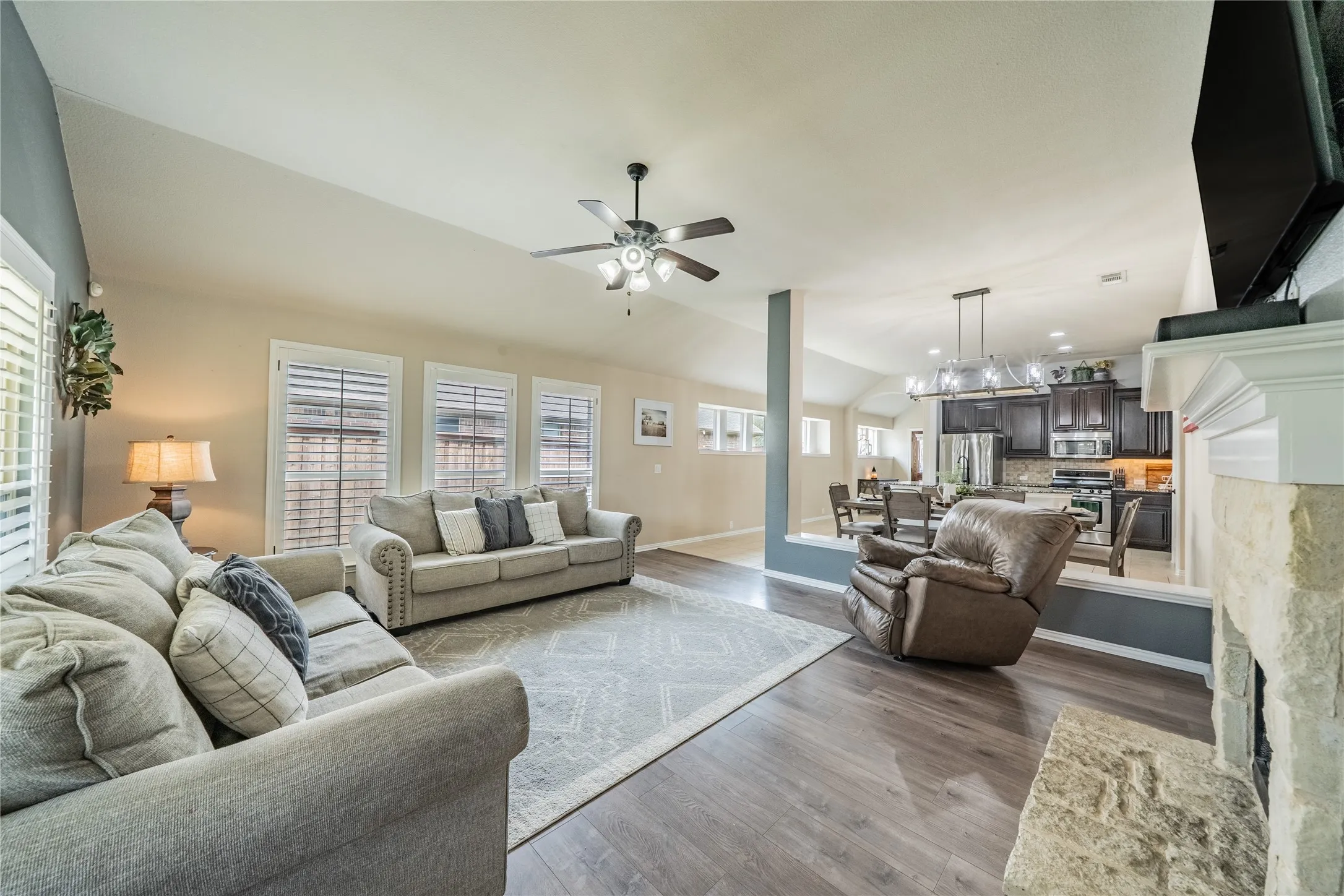 Spacious living area featuring vaulted ceilings, wood-finish flooring, a stone fireplace, and a ceiling fan
