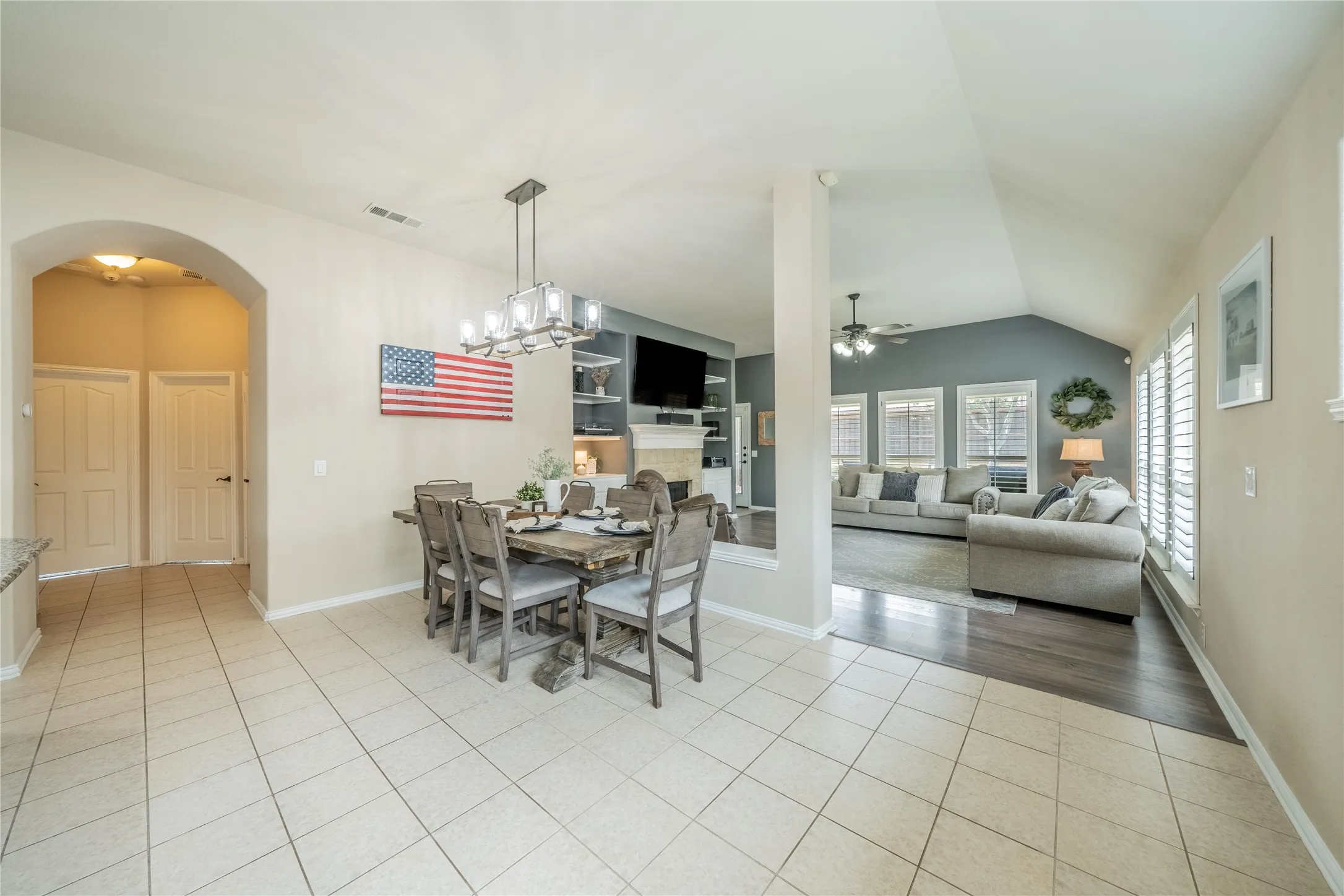 Vaulted ceiling living room with wood-finish flooring, plantation shutters, and a ceiling fan